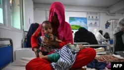 FILE - A woman sits on a hospital bed with her 4-month-old twins in the malnutrition ward at the Boost Hospital, run by Medecins Sans Frontieres, in Lashkar Gah, Helmand province, Afghanistan, July 21, 2022.