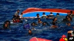 FILE - People swim next to their overturned wooden boat during a rescue operation by Spanish NGO Open Arms at south of the Italian Lampedusa island at the Mediterranean sea, Aug. 11, 2022.