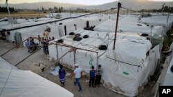 Syrian refugees walk by their tents at a refugee camp in the town of Bar Elias, in the Bekaa Valley, Lebanon, July 7, 2022.