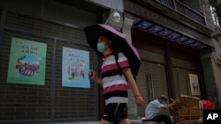 A man wearing a face mask and holding an umbrella to shield himself from the sun walks by an elderly man collecting recycle items in front of vacant shop lots at Qianmen Street in Beijing, Aug. 17, 2022.