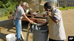 FILE - A worker with a construction and disaster relief firm, left, fills up a large garbage can with non-potable water for a local high school in Jackson, Mississipi, Aug. 31, 2022. Residents could use the water in their toilets, or for cleaning and laundry.