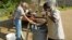 A worker with a construction and disaster relief firm, left, fills up a large garbage can with non-potable water for a local high school in Jackson, Mississipi, Aug. 31, 2022. Residents can use the water in their toilets, or for cleaning and laundry. 