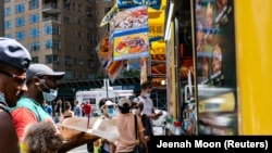 Warga AS yang memakai masker sedang membeli makanan dari pedagang kaki lima di dekat Central Park, di wilayah Manhattan, New York City, AS, 21 Juni 2020. (Foto: REUTERS/Jeenah Moon)