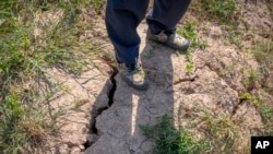 A farmer stands above a deep crack in the dried mud of an earthen embankment in his rice fields on the outskirts of Chongqing, China, Aug. 21, 2022.