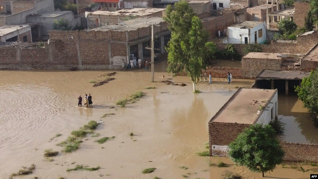 Warga mengarungi daerah yang dilanda banjir menyusul hujan lebat di distrik Charsadda di Khyber Pakhtunkhwa, Pakistan, 29 Agustus 2022. (Foto: AFP)