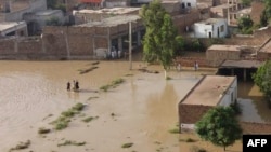 Warga mengarungi daerah yang dilanda banjir menyusul hujan lebat di distrik Charsadda di Khyber Pakhtunkhwa, Pakistan, 29 Agustus 2022. (Foto: AFP)