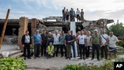 Volunteers pose for a group photo in front of Zhanna Dynaeva's and Serhiy Dynaev's house which was destroyed by Russian bombardment, in the village of Novoselivka, near Chernihiv, Ukraine, Aug. 13, 2022.