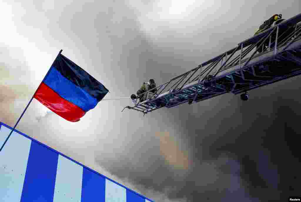 Firefighters work next to a flag of the self-proclaimed Donetsk People's Republic as they attempt to extinguish a fire at the shopping mall Galaktika following recent shelling in the course of Ukraine-Russia conflict in Donetsk, Ukraine.