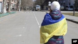FILE - A woman covered by Ukrainian flag stands in front of Russian troops in a street during a rally against Russian occupation in Kherson, Ukraine, March 19, 2022. 