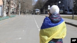 Seorang perempuan yang membawa bendera Ukraina berdiri dihadapan pasukan Rusia dalam aksi protes menentang pendudukan Rusia di jalanan kota Kherson, Ukraina, pada 19 Maret 2022. (Foto: AP)