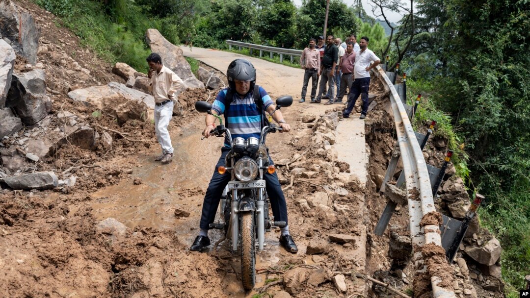 A motorcyclist tries to drive past mud and debris after a landslide blocked a road in Dharmsala, Himachal Pradesh state, India, Aug. 21, 2022.