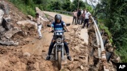 A motorcyclist tries to drive past mud and debris after a landslide blocked a road in Dharmsala, Himachal Pradesh state, India, Aug. 21, 2022.