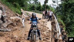 A motorcyclist tries to drive past mud and debris after a landslide blocked a road in Dharmsala, Himachal Pradesh state, India, Aug. 21, 2022.