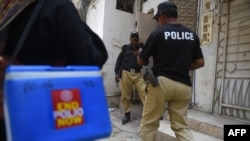 FILE - Policemen escort members of a polio vaccination team during a door-to-door vaccination campaign in Karachi, Pakistan, June 28, 2022.