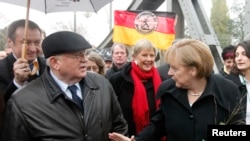 FILE - German Chancellor Angela Merkel, right, and former Soviet Union President Mikhail Gorbachev, left, chat as they walk through the Bornholmer Bridge in Berlin during celebrations to mark the 20th anniversary of the fall of the Berlin Wall, Nov. 9, 2009.