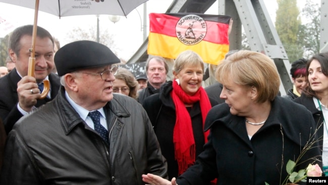 FILE - German Chancellor Angela Merkel, right, and former Soviet Union President Mikhail Gorbachev, left, chat as they walk through the Bornholmer Bridge in Berlin during celebrations to mark the 20th anniversary of the fall of the Berlin Wall, Nov. 9, 2009.