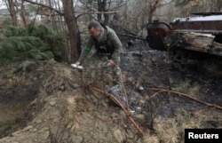 FILE - A military sapper picks up unexploded parts of a cluster bomb left after Russia's invasion near the village of Motyzhyn, in Kyiv region, Ukraine, April 10, 2022.