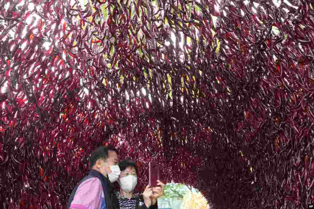 A couple wearing face masks takes a selfie photo inside a tunnel made with hot red peppers during H.O.T Festival at the Seoul City Hall plaza in Seoul, South Korea.