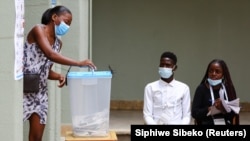 Une femme met son bulletin dans l'urne sous le regard des observateurs dans un bureau de vote de Luanda, en Angola, le 24 août 2022.