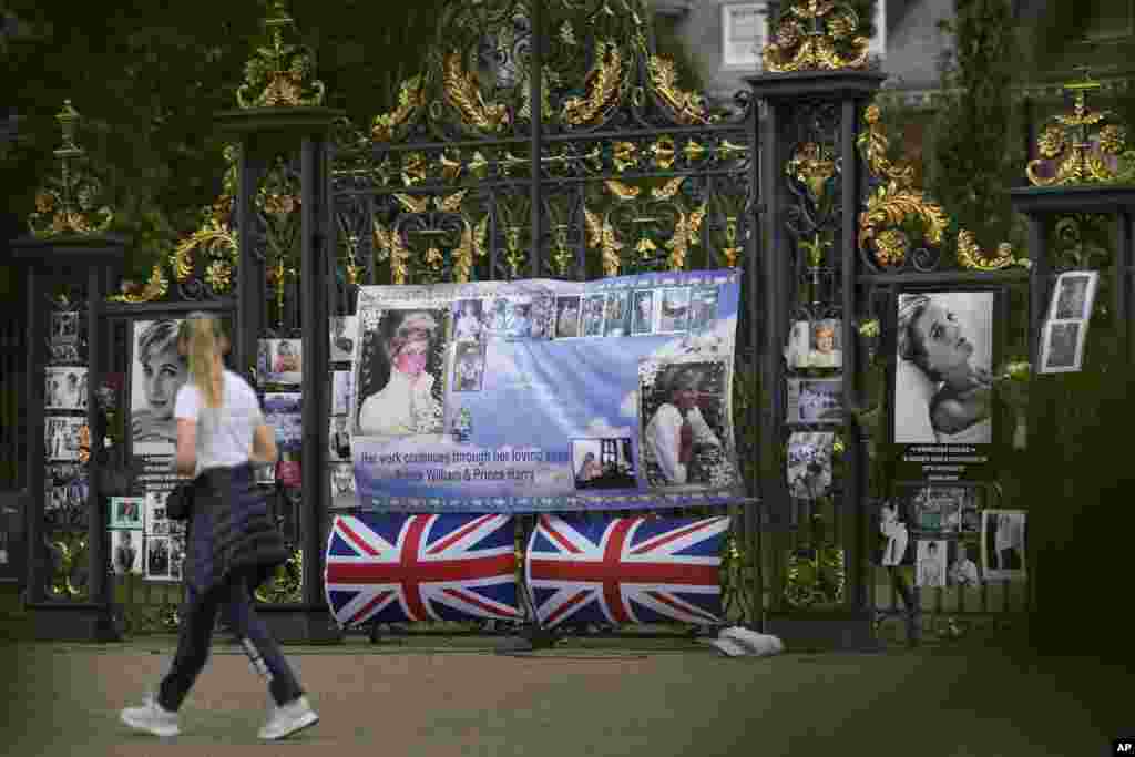 A woman walks by portraits of Princess Diana displayed on the gates of Kensington Palace, in London.