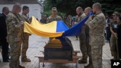 FILE - Soldiers hold a Ukrainian flag over the coffin of a soldier killed by Russian troops in battle, during his funeral at St. Michael cathedral in Kyiv, Ukraine, July 18, 2022.