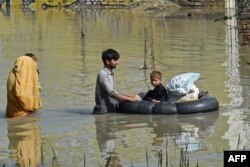 Sebuah keluarga mengarungi daerah yang dilanda banjir setelah hujan lebat di distrik Charsadda di Khyber Pakhtunkhwa, 29 Agustus 2022. (Foto: AFP)