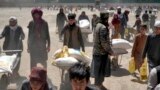 FILE - A Taliban fighter stands guard as people receive food rations distributed by a Chinese humanitarian aid group, in Kabul, Afghanistan, April 30, 2022. Afghanistan is expected 1.1 million children under the age of 5 will face malnutrition in the coun