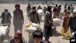 FILE - A Taliban fighter stands guard as people receive food rations distributed by a Chinese humanitarian aid group, in Kabul, Afghanistan, April 30, 2022. In Afghanistan 1.1 million children under the age of 5 will possibly face malnutrition this year.