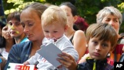 Refugees from Melitopol, Alena, 34, no surname name given, with her children Miron, 11, and Sabina, 2, wait in queue to receive food at a humanitarian aid distribution point in Zaporizhzhia, Ukraine, Aug. 11, 2022.