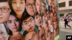 FILE - A woman walks past a banner with photos of pro-democracy activists, including Joshua Wong, center, during the anniversary of the Hong Kong handover to China from Britain in Hong Kong, July 1, 2021.