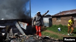 A resident gestures after the burning of shacks and belongings as mobs searched for alleged illegal miners in protest, following a gang rape of members of a video crew at a mine dump in the nearby township, in the West Rand, South Africa, Aug. 8, 2022.