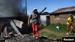 A local resident gestures after the burning of shacks and belongings as mobs searched for alleged illegal miners known as zama-zamas in protest, following an alleged gang rape of members of a video crew at a mine dump in the nearby township, in the West R