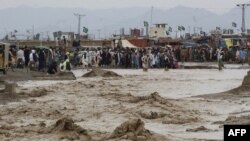 Orang-orang mengarungi banjir lumpur setelah hujan deras di kota perbatasan Chaman di Provinsi Balochistan pada 25 Agustus 2022. (Foto: AFP)