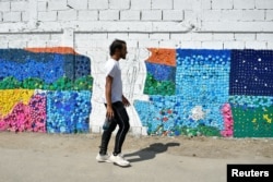 Seniman Venezuela Oscar Olivares berjalan melewati salah satu mural ramah lingkungan karyanya yang terbuat dari tutup botol untuk meningkatkan kesadaran akan daur ulang, di Caracas, Venezuela, 19 Agustus 2022. (REUTERS/Gaby Oraa) 