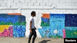 El artista venezolano Oscar Olivares pasa junto a un colorido mural ecológico que está creando con tapas de botellas para crear conciencia sobre el reciclaje, en Caracas, Venezuela, 19 de agosto de 2022. REUTERS/Gaby Oraa 