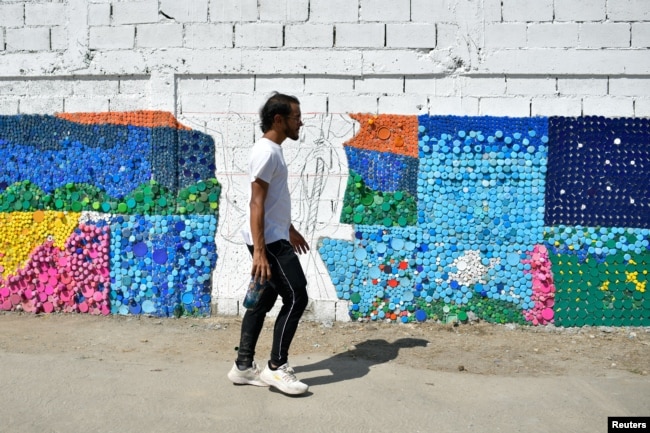Seniman Venezuela Oscar Olivares berjalan melewati salah satu mural ramah lingkungan karyanya yang terbuat dari tutup botol untuk meningkatkan kesadaran akan daur ulang, di Caracas, Venezuela, 19 Agustus 2022. (REUTERS/Gaby Oraa) 