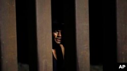 David, of Mexico, looks through the border wall as he collects recyclables and items left by migrants waiting along a border wall Aug. 23, 2022, near Yuma, Ariz. 