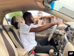 Adenekan Ayomide, 27, an undergraduate student turned a taxi driver following nationwide university strike, poses for a photograph inside his taxi in Abuja, Nigeria, Tuesday, May 10, 2022.