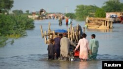 Men walk along a flooded road with their belongings, following rains and floods during the monsoon season in Suhbatpur, Pakistan, Aug. 28, 2022. (Reuters/Amer Hussain)