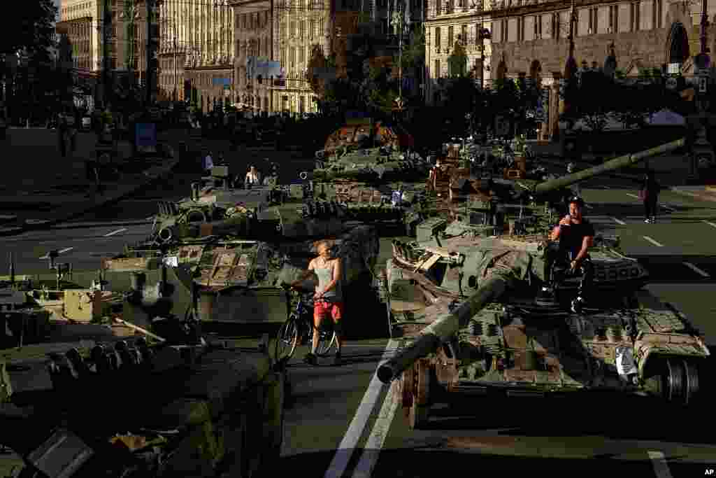 People walk around destroyed Russian military vehicles installed in downtown Kyiv, Ukraine. Kyiv authorities have banned mass gatherings in the capital through Thursday for fear of Russian missile attacks. Independence Day, like the six-month mark in the war, falls on Wednesday.