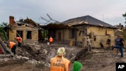 A worker arrives with a broom at a crater caused by a rocket strike on a house in Kramatorsk, Donetsk region, eastern Ukraine, Aug. 12, 2022. 
