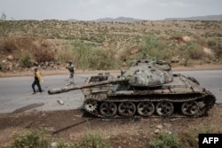 (FILES) Petani lokal berjalan di samping sebuah tank yang diduga milik tentara Eritrea yang ditinggalkan di sepanjang jalan di Dansa, barat daya Mekele di wilayah Tigray, Ethiopia, 20 Juni 2021. (Yasuyoshi CHIBA / AFP)