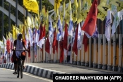 Seorang perempuan bersepeda melewati bendera partai politik jelang Pemilu 2019 di Banda Aceh, 23 Maret 2019. (Foto: AFP/CHAIDEER MAHYUDDIN)