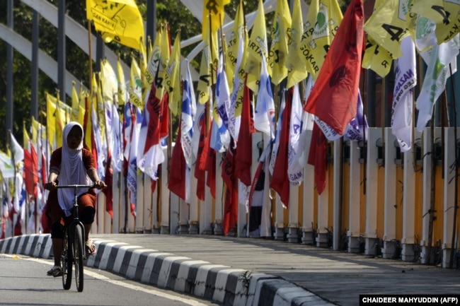 Seorang perempuan bersepeda melewati bendera partai politik jelang Pemilu 2019 di Banda Aceh, 23 Maret 2019. (Foto: AFP/CHAIDEER MAHYUDDIN)