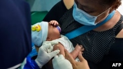 FILE - A mother holds her infant as a member of the medical staff administers the vaccination for tuberculosis at a community health center in Banda Aceh, Indonesia, on June 15, 2020. 