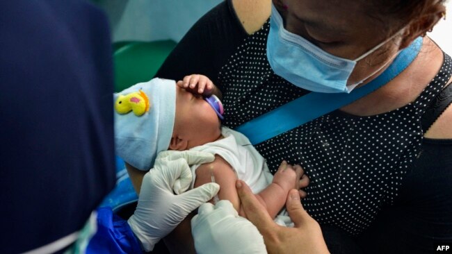 FILE - A mother holds her infant as a member of the medical staff administers the vaccination for tuberculosis at a community health center in Banda Aceh, Indonesia, on June 15, 2020.