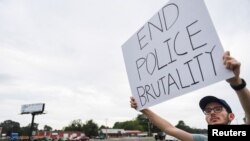 Miles Mason, 25, protests outside the sheriff's department where three Arkansas law enforcement officers have been suspended after a video circulated widely online over the weekend showing them punching and kicking a suspect.