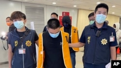 Petugas polisi dari Biro Investigasi Taiwan menggiring dua orang tersangka yang dideportasi dari Bangkok, ketika tiba di Bandara Internasional Taoyuan, Taiwan, pada 18 Agustus 2022. Keduanya diduga terlibat penipuan di Kamboja. (Taiwan Criminal Investigation Bureau via AP)