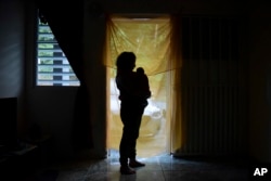 FILE - Michelle Flandez stands in her home with her two-month-old son Inti Perez, woh is diagnosed with microcephaly linked to the mosquito-borne Zika virus, in Bayamon, Puerto Rico on Dec. 16, 2016. (AP Photo/Carlos Giusti, File)