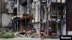 A woman walks near a building damaged in the course of Ukraine-Russia conflict in the southern port city of Mariupol, Ukraine, August 21, 2022.